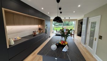 Open plan kitchen remodelling with dark cabinets and natural light from garden doors